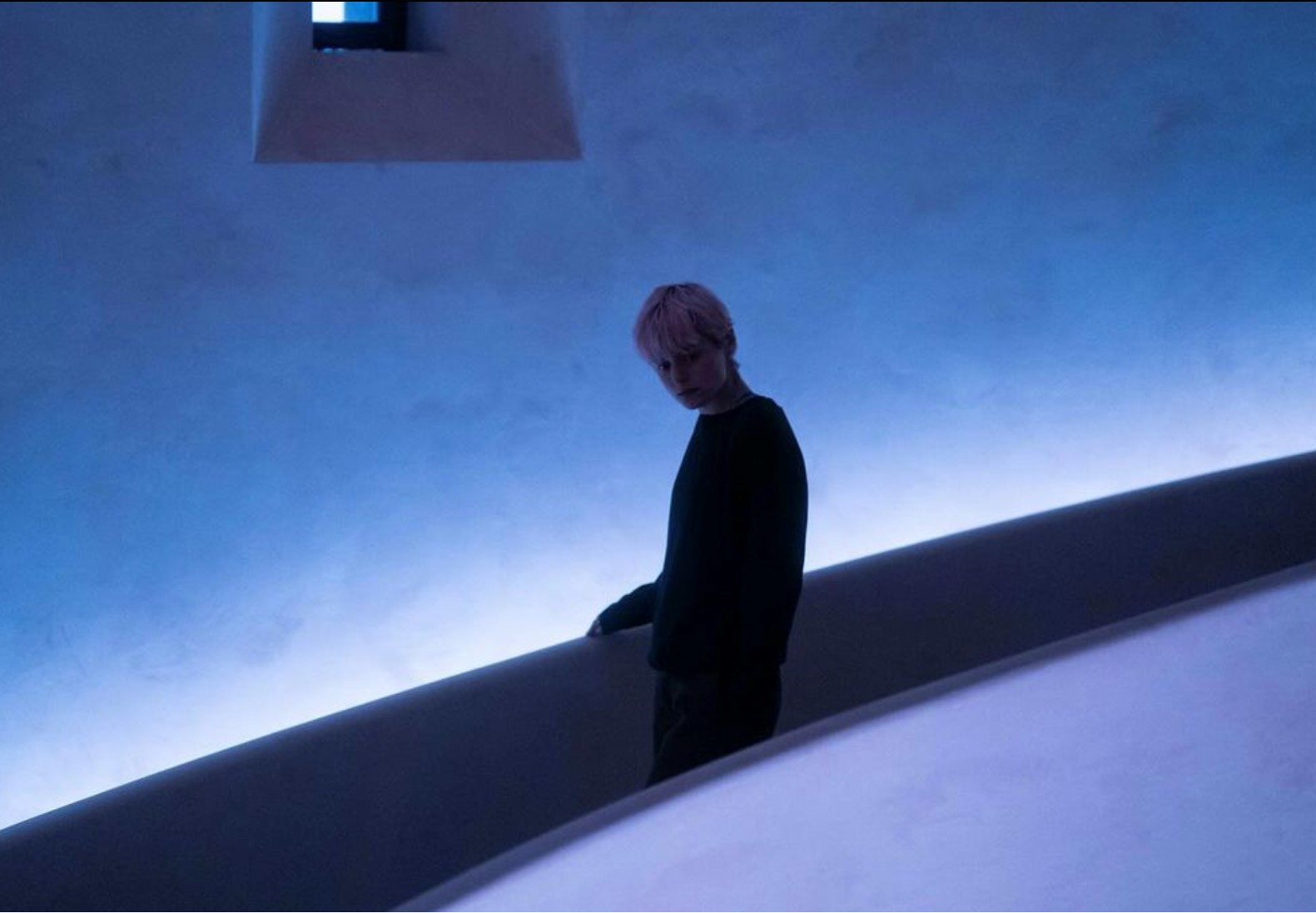 Darby Hart alone in a dimly lit blue plaster staircase
