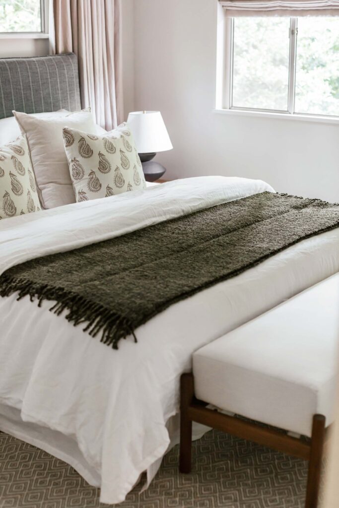 Guest room 2 close up of bed with neutral tones accent with gray-blue fabric headboard and moss colored chenille throw