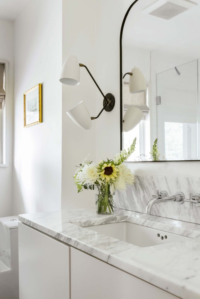 Guest bath in all white with marble counters and black lighting and mirror frame